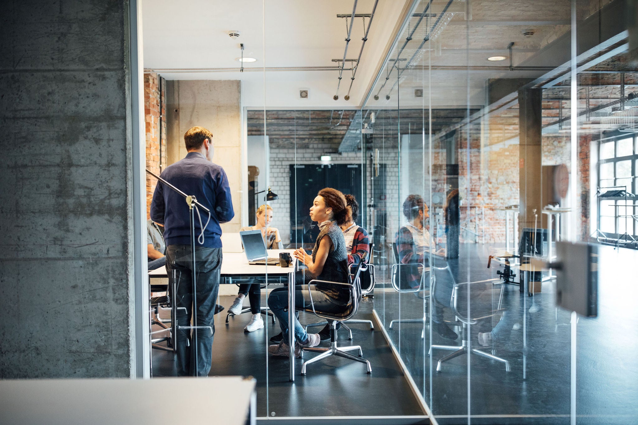 Businessman giving presentation to colleagues seen through glass doors at creative office